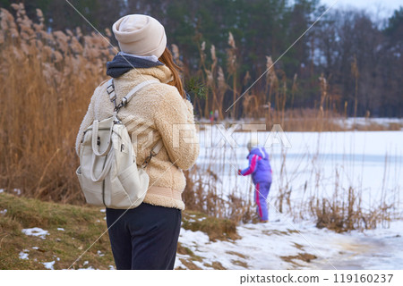 Mom and daughter walk on the shore of the winter frozen lake in the park Mom and daughter walk on the shore of the winter frozen lake in the park 119160237