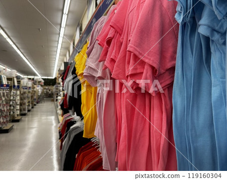 a display of brightly colored folded t-shirts on hangers in a well-lit store aisle 119160304