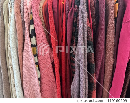 various textured sweaters in shades of pink, red, and beige hanging on a rack 119160309