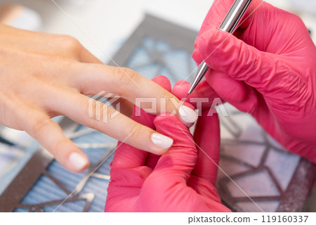 A manicurist carefully applies gel polish using a small brush to enhance the clients nails. A manicurist carefully applies gel polish using a small brush to enhance the clients nails. 119160337