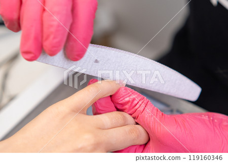 Skilled technician files nails carefully while providing a manicure to a client in a salon. Skilled technician files nails carefully while providing a manicure to a client in a salon. 119160346