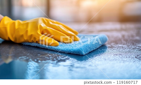 Close up of a woman's hand in yellow gloves cleaning a table with a blue microfiber cloth. 119160717