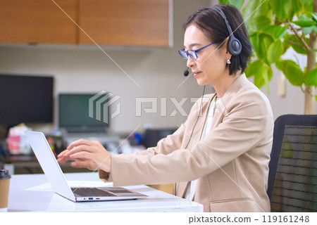 A middle-aged woman working in an office wearing a headset 119161248