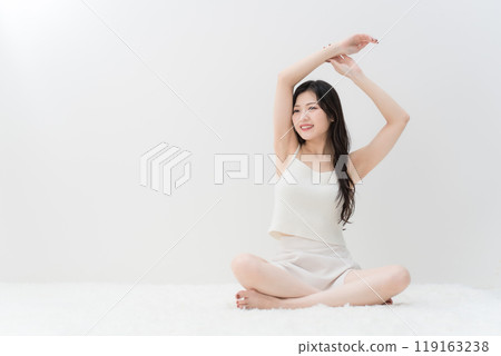 Beauty: A young woman stretching while sitting cross-legged Beauty: A young woman stretching while sitting cross-legged 119163238