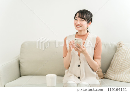 Japanese woman doing online shopping, reading, side job using smartphone on sofa at home 119164131