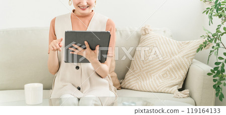 A smiling Japanese woman sitting on a sofa at home and studying, working, and using SNS on a tablet device A smiling Japanese woman sitting on a sofa at home and studying, working, and using SNS on a tablet device 119164133