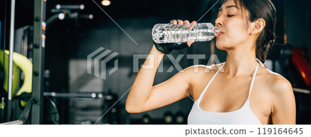 Asian woman guy hydrated by drinking water sports from a bottle in gym after cardio work out, female tired with liquid bottle drink after training at fitness gym, workout healthy lifestyle concept Asian woman guy hydrated by drinking water sports from a bottle in gym after cardio work out, female tired with liquid bottle drink after training at fitness gym, workout healthy lifestyle concept 119164645