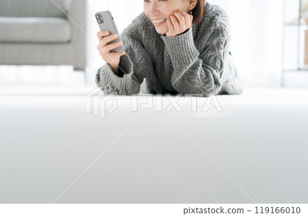 一個女人躺在地板上看著智慧型手機 一個女人躺在地板上看著智慧型手機 119166010