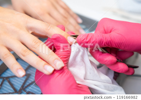 Nail technician trims the cuticles with cuticle nippers on a clients fingers in a stylish, modern nail salon. Nail technician trims the cuticles with cuticle nippers on a clients fingers in a stylish, modern nail salon. 119166982