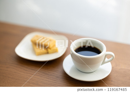 A cup of coffee placed on a table by a window with sunlight filtering through the trees A cup of coffee placed on a table by a window with sunlight filtering through the trees 119167485
