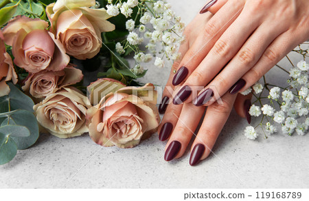 Elegant hands with dark nail polish resting beside fresh roses and delicate flowers 119168789