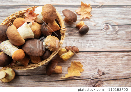 A woven basket filled with various mushrooms and autumn leaves on a wooden surface A woven basket filled with various mushrooms and autumn leaves on a wooden surface 119168790