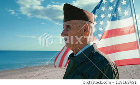 United States Veteran Looks At The Ocean From The Beach With America Flag 119169451