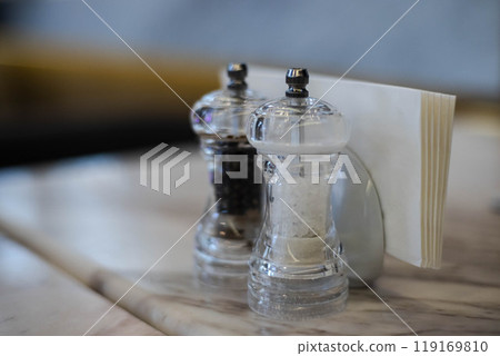 Charming table setting with salt and pepper shakers beside a folded napkin in a cozy dining atmosphere Charming table setting with salt and pepper shakers beside a folded napkin in a cozy dining atmosphere 119169810