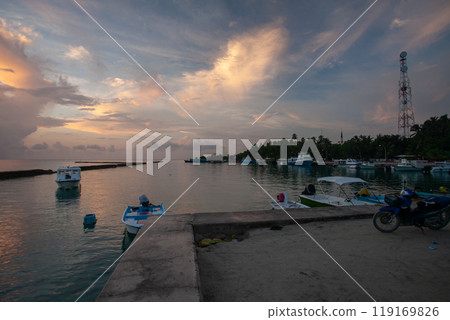 Serene sunset over Maldives harbor with fishing boats gently swaying on calm waters Serene sunset over Maldives harbor with fishing boats gently swaying on calm waters 119169826