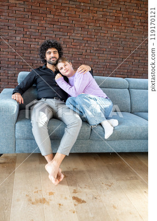 A couple is cozy on a sofa in a modern living room, showing affection towards each other 119170121