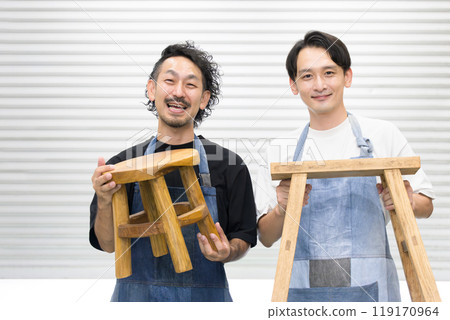 Two male craftsmen looking at the camera while doing DIY, cutting wood, crafting and carving - Image of a carpenter or woodworker 119170964