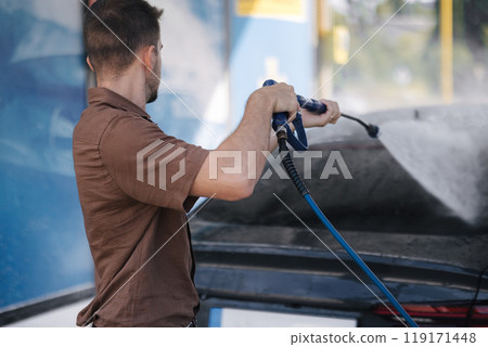 Handsome man washes his luxury car at a self-service car wash. Water under pressure Handsome man washes his luxury car at a self-service car wash. Water under pressure 119171448