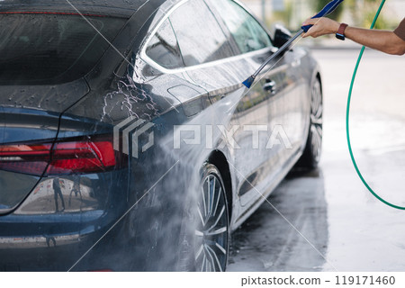 Handsome man washes his luxury car at a self-service car wash. Water under pressure Handsome man washes his luxury car at a self-service car wash. Water under pressure 119171460