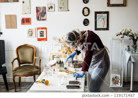 Artist preparing resin mixture in a home art studio, wearing protective gear. Essential tools and materials for setting up a functional creative workspace. Artist preparing resin mixture in a home art studio, wearing protective gear. Essential tools and materials for setting up a functional creative workspace. 119171487