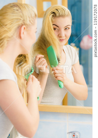 Woman brushing her blonde hair in bathroom Woman brushing her blonde hair in bathroom 119172078