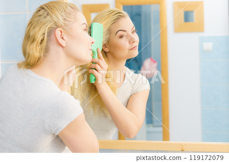 Woman brushing her blonde hair in bathroom Woman brushing her blonde hair in bathroom 119172079