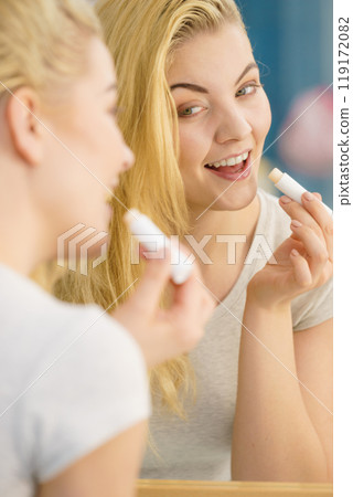 Woman in bathroom applying lip balm Woman in bathroom applying lip balm 119172082