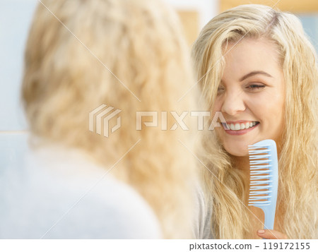 Woman getting ready in bathroom, combing hair. Woman getting ready in bathroom, combing hair. 119172155