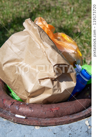 A brown paper bag sits atop a trash can next to a fire hydrant and some grass 119173720