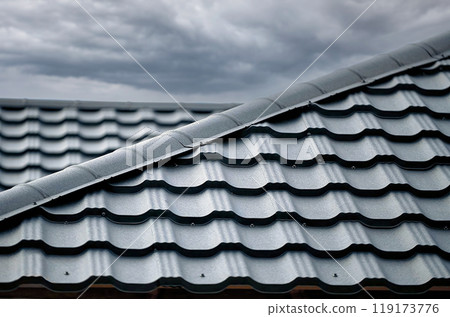 Close-up house roof with steel roofing sheet. Gray modular tile effect roof panel. Traditional metal shingle tiles. Profiled metallic corrugated pantile as clay or concrete slate. Building's covering Close-up house roof with steel roofing sheet. Gray modular tile effect roof panel. Traditional metal shingle tiles. Profiled metallic corrugated pantile as clay or concrete slate. Building's covering 119173776