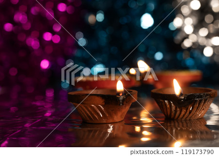Glowing Diwali diyas with beautiful light reflection on the ground with bokeh effect in dark background. 119173790