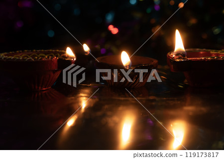 Glowing Diwali diyas with beautiful light reflection on the ground with bokeh effect in dark background. 119173817