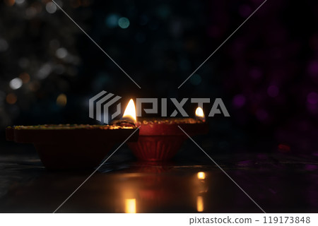 Glowing Diwali diyas with beautiful light reflection on the ground with bokeh effect in dark background. Closeup 119173848
