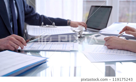 Business people wearing blue suits are reviewing financial data in office. Two professionals analyzing paper reports using calculators. Audit and taxes concept Business people wearing blue suits are reviewing financial data in office. Two professionals analyzing paper reports using calculators. Audit and taxes concept 119175243