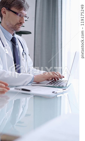 Male physician in white coat focused on laptop data in a modern clinic office while analyzing patient information on laptop. Medicine concept 119175249
