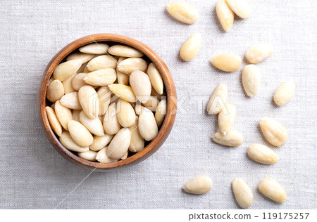 Freshly blanched almonds in a wooden bowl on linen. Shelled almonds that have been treated with hot water to soften the seed coat, which is then removed to reveal the seed. Fruits of Prunus amygdalus. 119175257