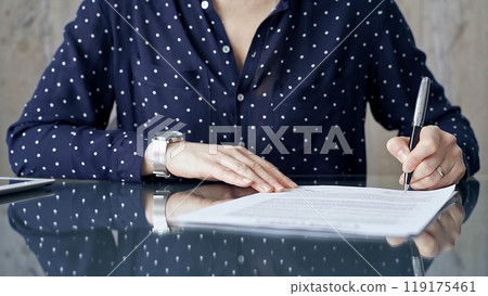 Businesswoman is signing corporate contract at her office desk in formal dark blue blouse with polka dots. Business people concept Businesswoman is signing corporate contract at her office desk in formal dark blue blouse with polka dots. Business people concept 119175461