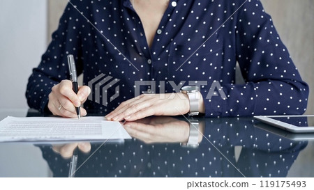 Businesswoman is signing corporate contract at her office desk in formal dark blue blouse with polka dots. Business people concept 119175493