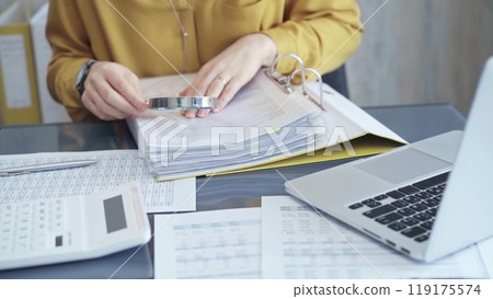 Female auditor in business attire inspecting financial reports with magnifying glass, surrounded by documents and a laptop and calculator. Business audit and taxes concept Female auditor in business attire inspecting financial reports with magnifying glass, surrounded by documents and a laptop and calculator. Business audit and taxes concept 119175574