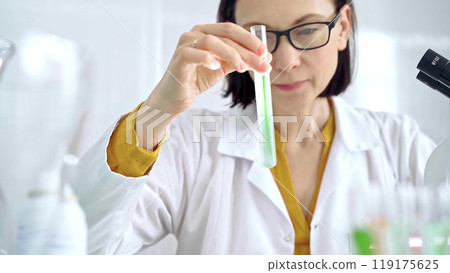 Scientist examining lab tube with a green fluid. Microbiology and science concept Scientist examining lab tube with a green fluid. Microbiology and science concept 119175625