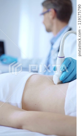 Doctor man wearing a blue protective gloves using an ultrasound machine on a female patient examining internal organs. Medicine concept Doctor man wearing a blue protective gloves using an ultrasound machine on a female patient examining internal organs. Medicine concept 119175790