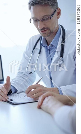 Doctor and a patient. The physician, wearing a white medical coat over a blue shirt, gesturing with his hands during a consultation in the clinic. Medicine concept 119175865