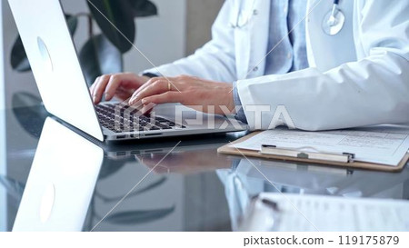 Doctor man with blue shirt and medical coat is using laptop computer in clinic office while sitting at the glass desk. Medicine concept 119175879