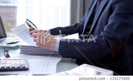Businessman reviewing ring folder of financial documents with magnifying glass at desk in modern office. Audit and taxes in business 119175880
