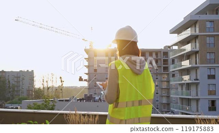 Construction female engineer taking notes and tapping on tablet computer while inspecting a building site at sunset. Industry development concept 119175883