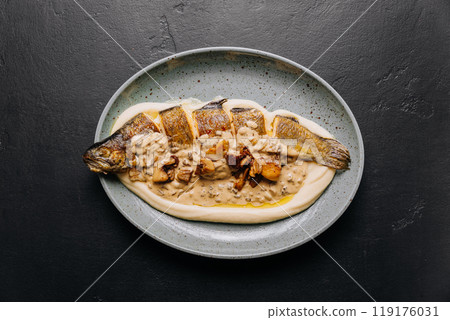 Whole roasted fish with creamy mushroom sauce and mashed potatoes on a ceramic plate 119176031