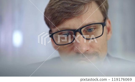 Businessman with glasses looking intently obscured partially by a translucent surface of laptop. Business concept Businessman with glasses looking intently obscured partially by a translucent surface of laptop. Business concept 119176069