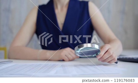 Businesswoman holding magnifying glass analyzing financial documents at office desk. Taxes, audit in business 119176083