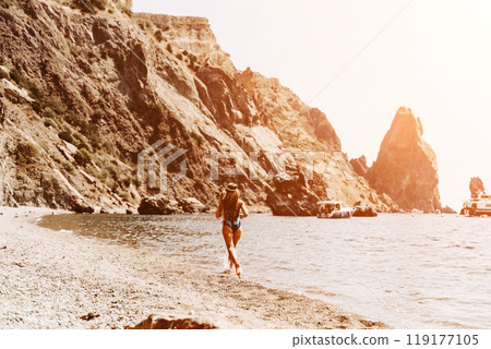 Woman travel summer sea. A happy tourist in a blue bikini enjoying the scenic view of the sea and volcanic mountains while taking pictures to capture the memories of her travel adventure. Woman travel summer sea. A happy tourist in a blue bikini enjoying the scenic view of the sea and volcanic mountains while taking pictures to capture the memories of her travel adventure. 119177105