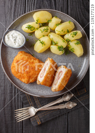 Classic cordon bleu with new potatoes and cream sauce close-up on a plate. Vertical top view Classic cordon bleu with new potatoes and cream sauce close-up on a plate. Vertical top view 119177119